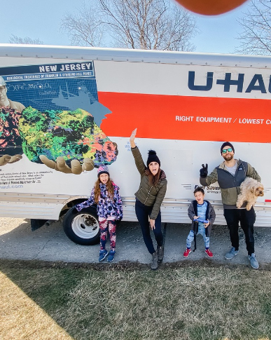 Family of 4 standing in front of their packed U-Haul truck on a chilly morning