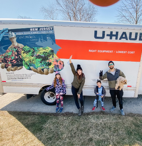 Family of 4 standing in front of their packed U-Haul truck on a chilly morning